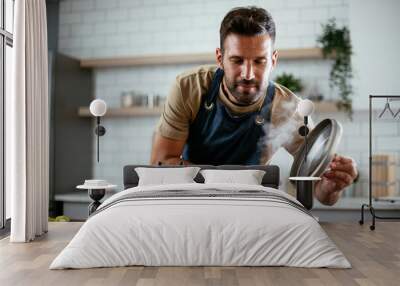 Handsome man preparing pasta in the kitchen. Guy cooking a tasty meal.. Wall mural