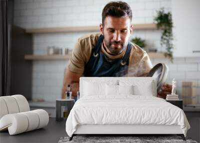 Happy man in kitchen. Young man preparing delicious food.. Wall mural