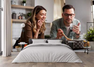 Happy smiling couple cooking together. Boyfriend and girlfriend preparing delicious food. Wall mural