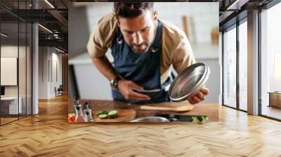 Happy smiling man preparing tasty meal. Young man cooking in the kitchen. Wall mural