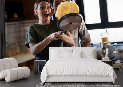 Husband and wife making pancakes at home. Young couple having fun in the kitchen. Wall mural