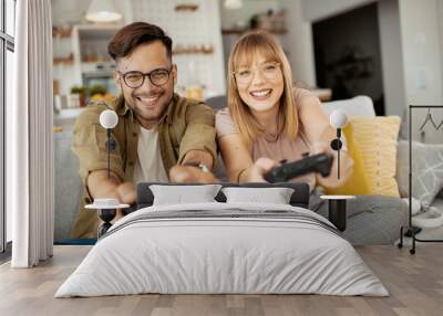 Husband and wife playing video game with joysticks in living room. Loving couple are playing video games at home.	 Wall mural