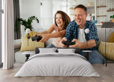 Husband and wife playing video game with joysticks in living room. Loving couple are playing video games at home. Wall mural