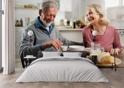 Senior couple eating breakfast in the kitchen. Husband and wife talking and laughing while eating a sandwich.. Wall mural