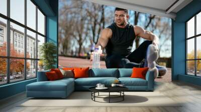 Thirsty athlete. Man reaching for a bottle of water. Guy trains outdoors. Wall mural