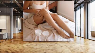 Woman applying body cream on her leg in bedroom. Close up Wall mural