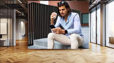 Young man sitting on the stairs drinking coffee. Handsome businessman talking to the phone while drinking coffee.. Wall mural