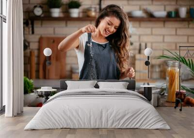 Young woman in kitchen. Beautiful woman having fun while making  dough. Wall mural