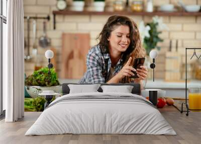 Young woman in kitchen. Beautiful woman using phone Wall mural