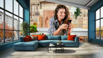 Young woman in kitchen. Beautiful woman using phone Wall mural