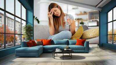 Young woman sick in bed holding glass of water.. Wall mural