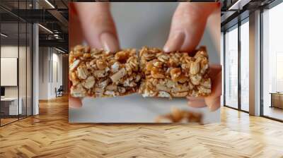 A womans hands breaking a buckwheat breakfast bar in half revealing its chewy and flavorful interior. Wall mural