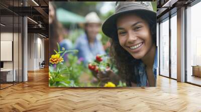 Closeup of a group of young adults in a community garden smiling as they work together to plant flowers and vegetables. . Wall mural