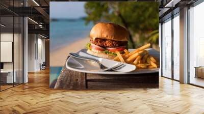 Large hamburger and chips served on a cafe table with sea views. Vacation and fast food Wall mural