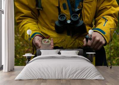 the man went hiking in the forest. In his hands he holds a compass, binoculars and a trekking stick close-up Wall mural