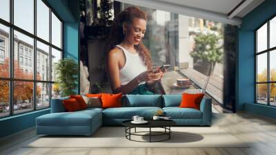 Woman entrepreneur with phone in a coffee shop, restaurant or cafe on social media app online. Happy and young freelance worker doing remote work planning on a mobile 5g smartphone internet schedule Wall mural