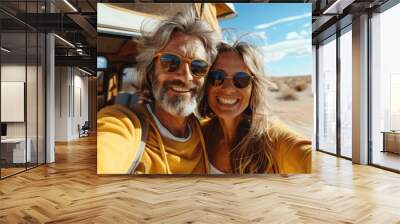 Happy couple taking a selfie while traveling in New Mexico desert, wearing sunglasses and yellow sweatshirt, vintage camper van in background Wall mural