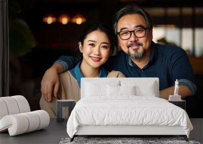 An Asian couple in their thirties sitting on the couch, happy and smiling at the camera, with a modern living room background Wall mural