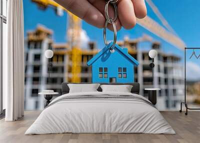 Keychain in house shape and key in male hand on background of construction cranes and new buildings Wall mural