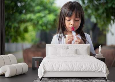 A young girl is blowing bubbles with a bubble wand. Wall mural