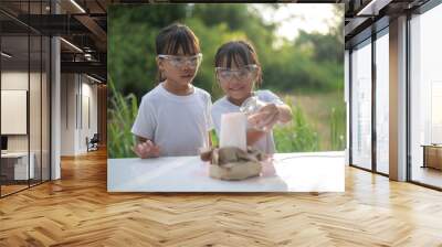 Two young girls excitedly play with a small volcano experiment, laughing as foam erupts. Wall mural