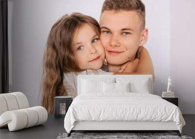 caucasian happy adorable siblings - teenager boy brother and little girl sister cuddling on white background indoor. Family, relationships, relatives, love, support concept Wall mural