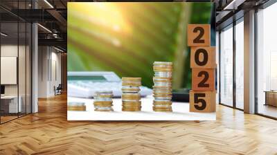 pile of coins and wooden blocks with numbers 2025, calculator, laptop and forest in the background Wall mural