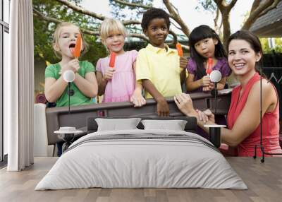 Preschool children on playground with teacher eating popsicles Wall mural