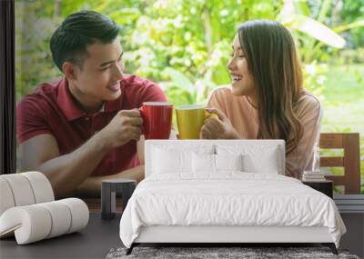 Cheerful young couple holding cup of coffee or tea while sitting on chair in the garden at home. Romantic lover enjoying drink hot mug mocha on the cup glass together in the morning. Wall mural