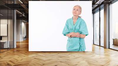 Pensive unhappy grandmother wear patient uniform looking copy space thinking worried problem standing over isolated white background. Insurance health care retired elderly woman troubled pain health. Wall mural