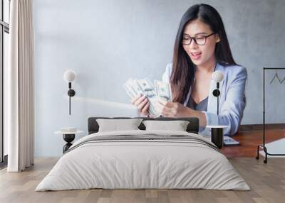 Beautiful business woman sitting at home office desk  using a laptop and smiling while working with banknote hold in hand, and and be attractive cheerful model using computer. Indoors Wall mural