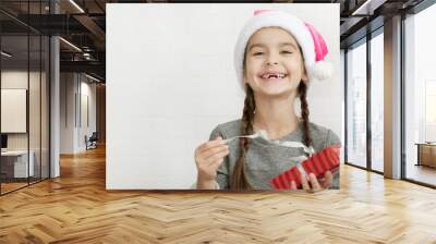 Happy adorable child girl in santa hat with christmas gift in hands in studio Wall mural