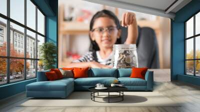 Asian little girl in putting coin in to glass jar shallow depth of field select focus at the jar Wall mural