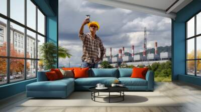 Man wearing a yellow hat was photographing himself with a power plant in the background Wall mural