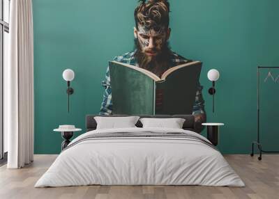 A tattooed man in a blue and green plaid shirt reads a green book against a teal background, conveying a sense of knowledge, wisdom, and individuality. 
 Wall mural