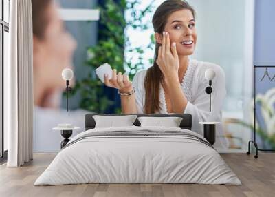 Beautiful brunette woman applying face cream in the bathroom Wall mural