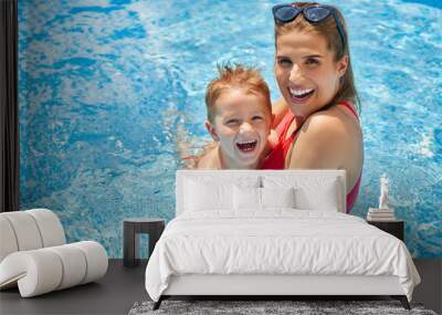 Cute boy with his mother playing in swimming pool during summer Wall mural