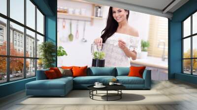 Fit smiling young woman preparing healthy smoothie in modern kitchen Wall mural