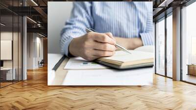 A woman is taking notes in a notebook, she works from home due to the epidemic, she records details of tasks assigned by her supervisor through a video conference. The idea of working from home. Wall mural