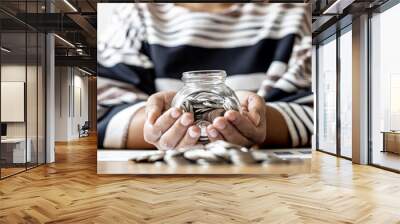 A woman is using two hands holding a glass jar with lots of coins inside, she has an income and expense accounting to plan her finances. Personal accounting ideas. Wall mural