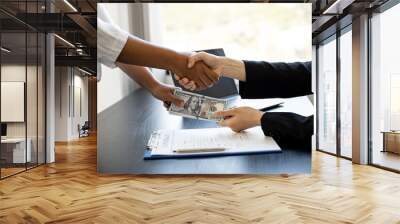 Two business women are shaking hands after negotiating a business jointly and giving away a large sum of dollars, a handshake is a Western greeting or congratulation. The concept of corruption. Wall mural