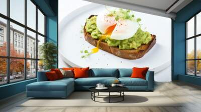 Delicious avocado toast topped with perfectly poached egg, served on a white plate for a fresh and healthy meal option. Wall mural