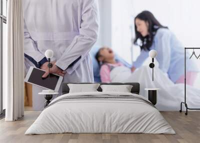 The doctor with tablet on hand for diagnosing the illness for a little girl on the hospital bed with mom beside. Wall mural