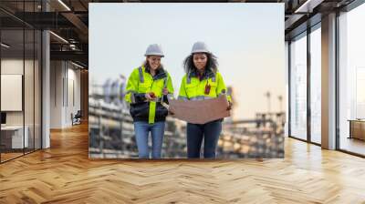 Two Engineers Reviewing Blueprint Plans at Industrial Facility, Wearing Safety Helmets and High-Visibility Jackets During a Site Inspection Wall mural