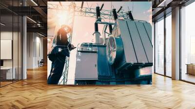 Businessman wearing a black suit, standing looking at a large power transformer with orange sunlight and white sky to be background, Concept about business people who want to invest in energy Wall mural