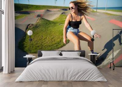 Attractive young woman riding longboard. Pretty sporty girl in sunglasses with skateboard on special riding area, doing trick. Sport, hobby, active lifestyle concept Wall mural