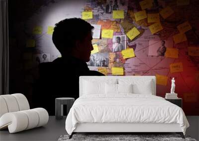 Back view of man planning in dark room. Unrecognizable man standing near wall with stickers, photographs and red threads. Planning, conspiracy concept Wall mural