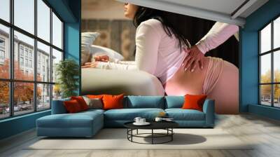 Cropped image of kneeling pregnant woman and midwife at home. Woman in casual clothes leaning on bed, Asian doula massaging back. Pregnancy, medicine, home birth concept Wall mural