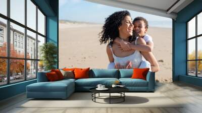 Joyful mother and son spending time on beach. African American family walking, laughing, playing, riding on back. Leisure, family time, parenthood concept Wall mural