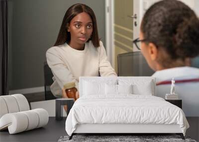 Serious African American woman listening to doctor in clinic. Female doctor talking to patient and showing pills. Medical consultation concept Wall mural